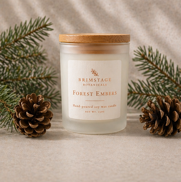 Brimstage Botanicals Forest Embers candle with lid sat next to pine cones and sprigs of freshly cut pine