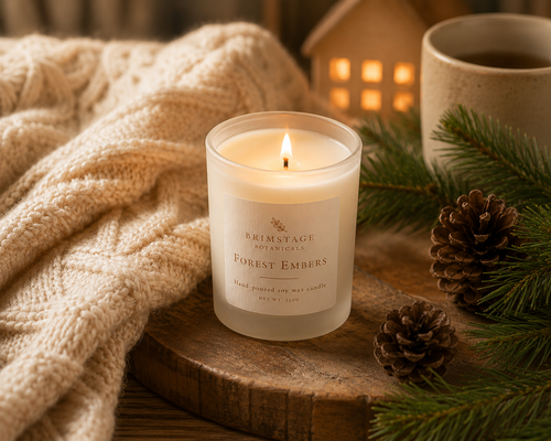 Warming scene with a lit Brimstage Botanicals Forest Embers soy wax candle, cozy blanket, and festive decor on a wooden surface.